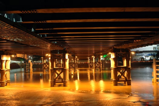 Bridge by night, photo taken under the bridge showing bridge's pillars and reflections from water. Ningbo city, China.