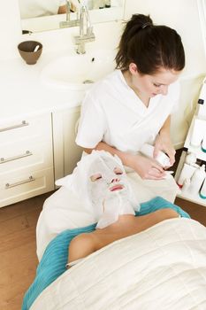Lotion being applied to the face during a facial mask at a beauty spa.