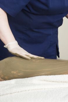 Sea mud for a full body wrap being applied to a leg a luxury spa.