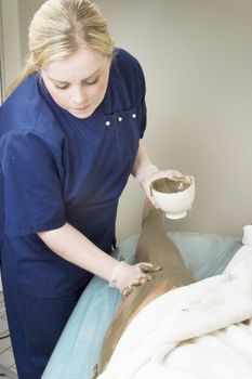 Sea mud for a full body wrap being applied to a leg a luxury spa.