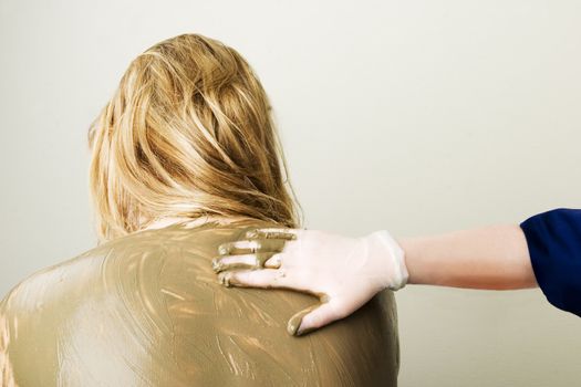 A sea mud full body wrap at a luxury spa being applied to the back and shoulders.