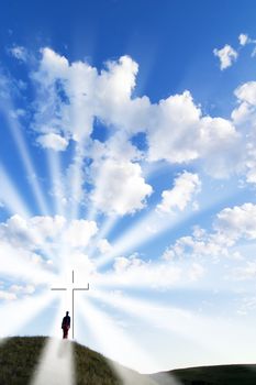 A person walking up to a glowing cross on a hill.
