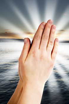 Praying hands with a landscape with the ocean and a sunset in the background