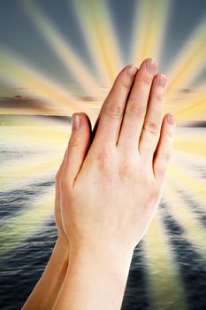 Praying hands with a landscape with the ocean and a sunset in the background.
