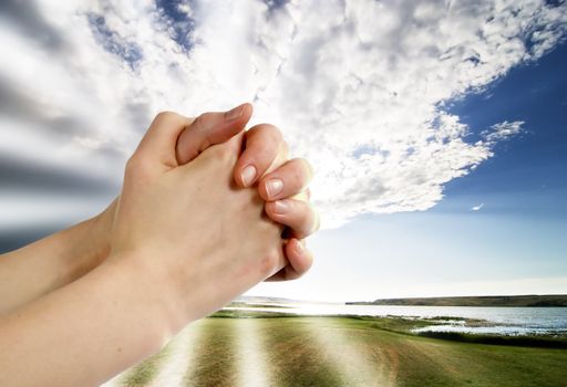 A pair of hands in a praying position set against a beautiful prairie lake landscape