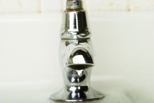 A retro sink tap and faucet.  A detail image of a water drip getting ready to drop.