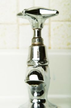 A retro sink tap and faucet with a drip gathering on the end.
