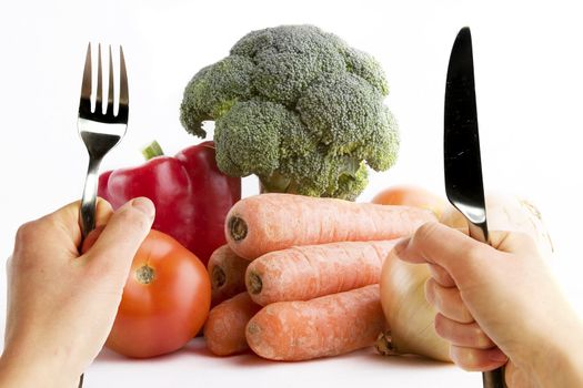 Group of raw vegetables on a white background with two hands in the foreground very eager to eat the food.