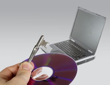 A hand holding a cd and skeleton key, with a laptop computer in the background.