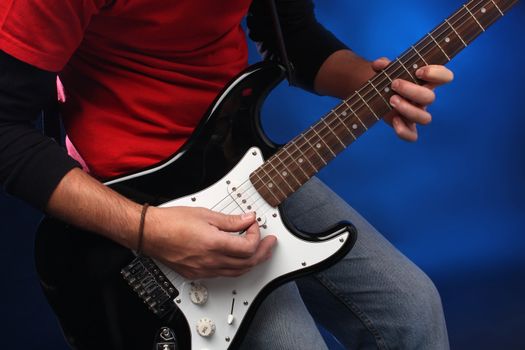 Detail of a musician playing a black electric guitar.