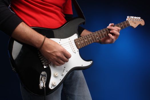 Detail of a musician playing a black electric guitar.