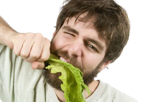 A young male with a beard is eagerly eating salad, as if he were a barbarian eating meat.