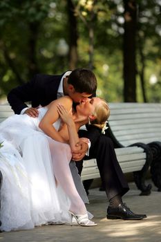 Newlywed couple kissing on park bench.