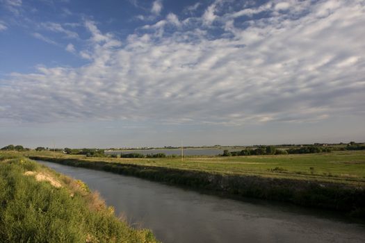 irrigation channel full of water, reservoir, and green meadows of north eastern Colorado farmland in late summer