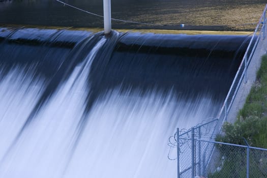 detail of river dam spillway (Idylwidle on Big Thompson, Colorado) with a fence and barbed wire in a blue shadow of deep canyon