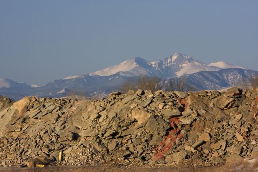 piles of concrete and construction waste obscure a view to snowy peaks of Rocky Mountains (Longs Peak in Colorado)