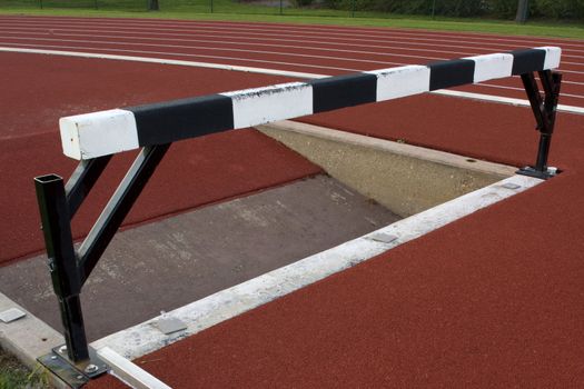 red running tracks with white and black steeplechase barrier and water jump pit