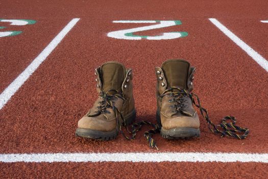 heavy hiking boots at starting line on a running track, concept - wrong equipment for a job