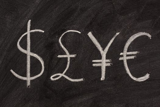 dollar, pound, yen and euro symbols sketched with white chalk on a black board