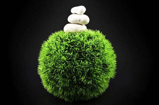 Three stones over a grass plastic ball, isolated on black