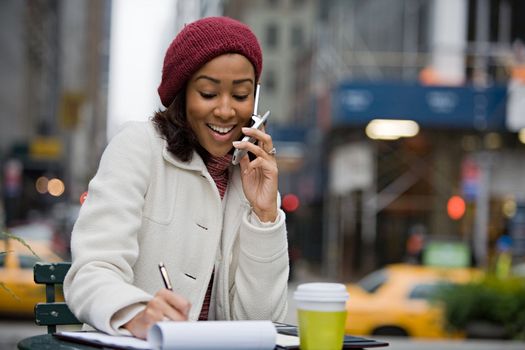 An attractive business woman talking on her cell phone while seated outdoors in the city.