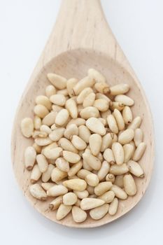 Pine nuts in a wooden spoon on a light background with light shadow and reflection. 

