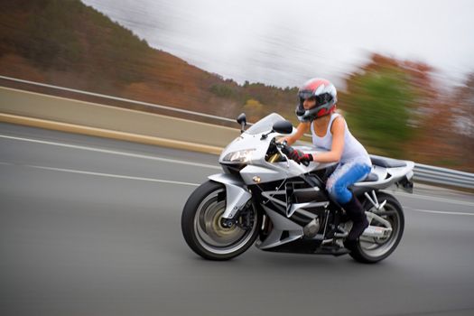 A pretty blonde girl in action driving a motorcycle at highway speeds.