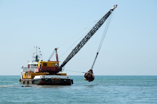 A barge is dredging a harbor removing stones and sand