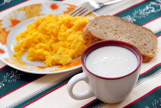 yoghurt in cup and scrambled eggs with bread served on table