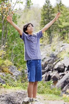 Teenage boy raising hands in praise to God outdoors on mountain