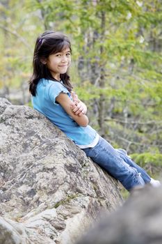 Little girl sitting against rock, smiling  over shoulder