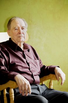 Elderly man in rocking chair looking out sunny window