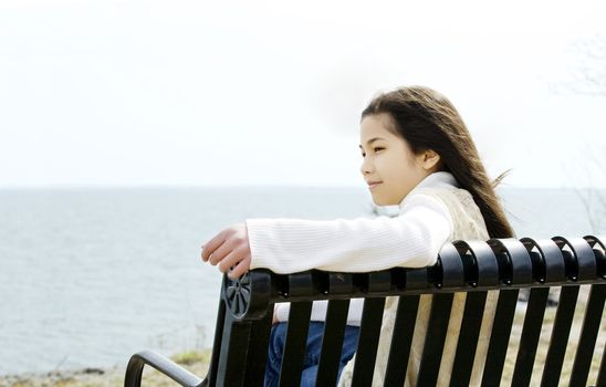 Little girl on bench by lake shore in beautiful sunshine