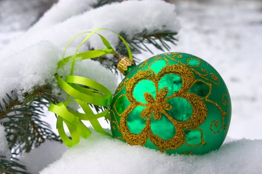 A green christmas bauble sitting in a bed of snow.