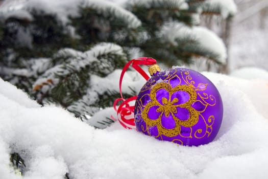A violet christmas bauble sitting in a bed of snow.