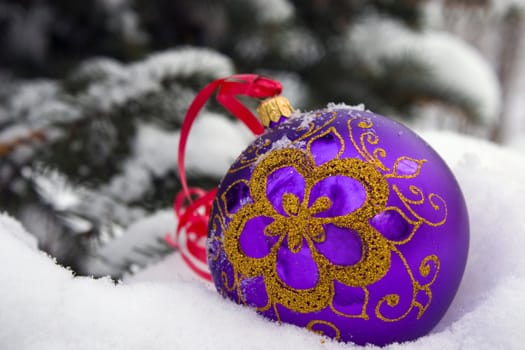 A violet christmas bauble sitting in a bed of snow.