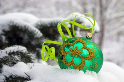 A green christmas bauble sitting in a bed of snow.