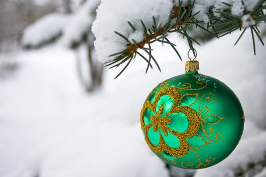 Green  christmas glass ball hanging on the tree in snow.