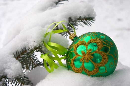 A green christmas bauble sitting in a bed of snow.