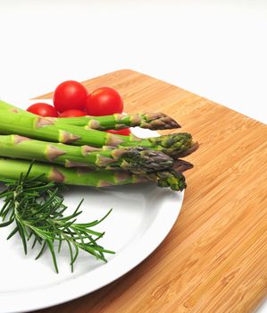 Asparagus spears on a white plate with cherry tomatoes and thyme