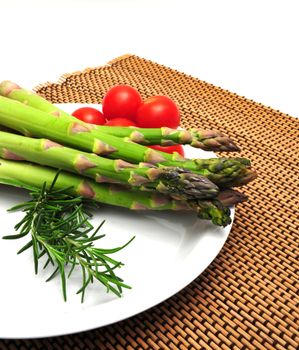 Asparagus and cherry tomatoes on a white saucer and wooden place mat