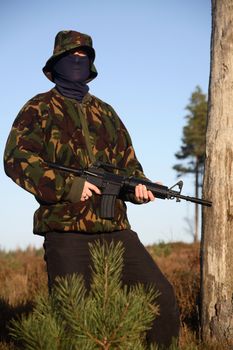 A soldier holding a M16 (AR-15) Rifle with camouflage and a balaclava.