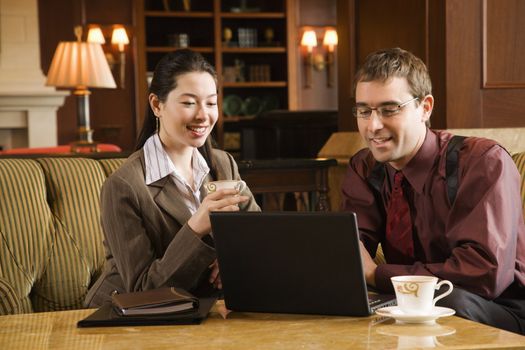 Caucasian mid adult businessman and woman drinking coffee and looking at laptop computer.