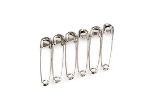 Six silver safety pins on white background