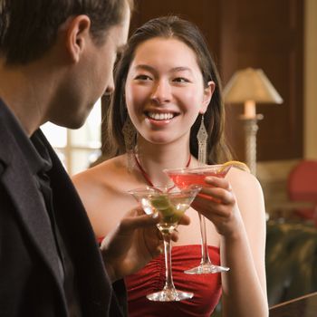 Taiwanese mid adult woman and Caucasian man toasting martinis.
