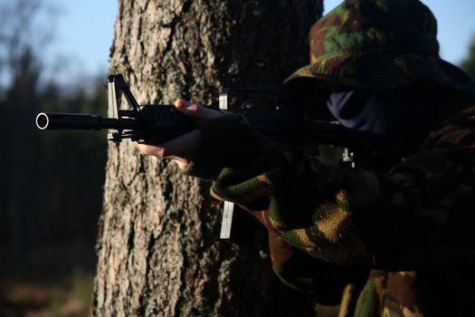 A soldier behind a tree, holding a rifle.
