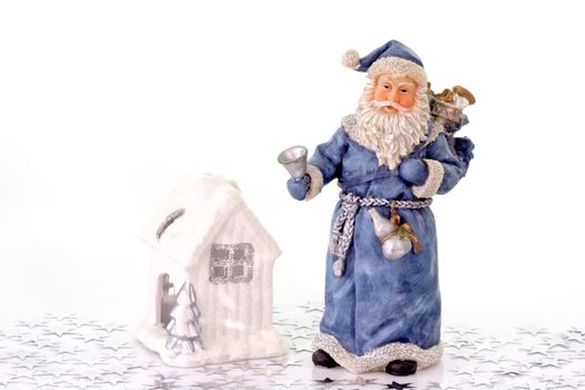 Blue Santa Claus figure with white ceramic house and silver stars on light background