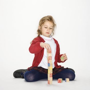 Studio portrait of Caucasian girl playing with toy blocks against white background.