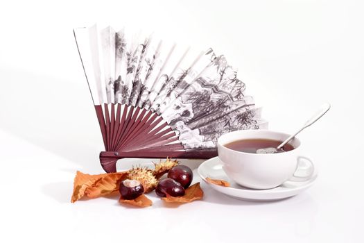 A cup of tea with fan and autumn foliage on bright background