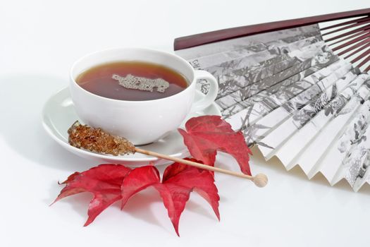 A cup of tea with fan and autumn leafs on bright background